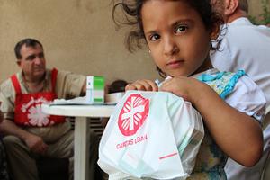 In eastern Lebanon, a Syrian refugee child holds free medicine given to her as part of a Caritas "mobile clinic" visit. Many refugee families are living in unsanitary conditions; children come to the doctor (left) because of diarrhea, coughing, lice, and other problems. Credits: Laura Sheahen/Caritas