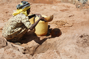 In southern Kenya, a woman uses a gourd to scoop water from a dry riverbed. During droughts, many women walk hours to find water. Credits: Laura Sheahen/Caritas