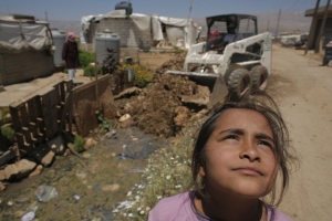 Une jeune réfugiée syrienne regarde comment un tracteur verse du sable dans une fosse septique, dans un camp tenu par Caritas dans la vallée de la Bekaa. Photo: Matthieu ALEXANDRE for CARITAS INTERNATIONALIS