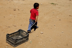 Un niño sirio juega con una caja de plástico cerca de un campamento de refugiados en Líbano. Foto: Matthieu Alexandre para Caritas Internationalis