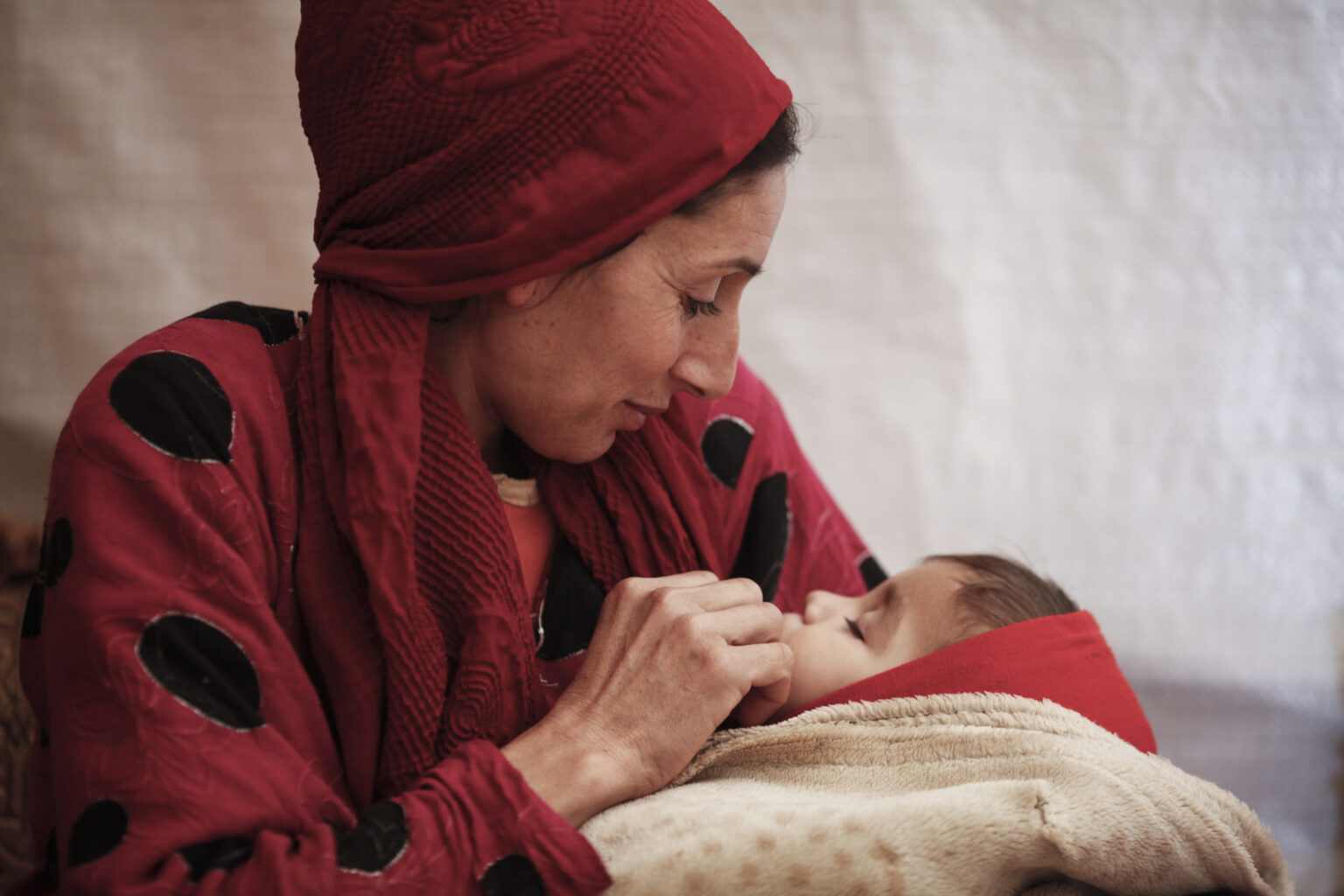 Souad Mohamed from Shaeeb al Dakr near Raqqa, Syria,  shelters from the cold with her her baby Hassan inside the tent in which they now live in an informal tented settlement in Kafr Zabat, in Lebanon's Bekaa Valley, on December 17, 2013.